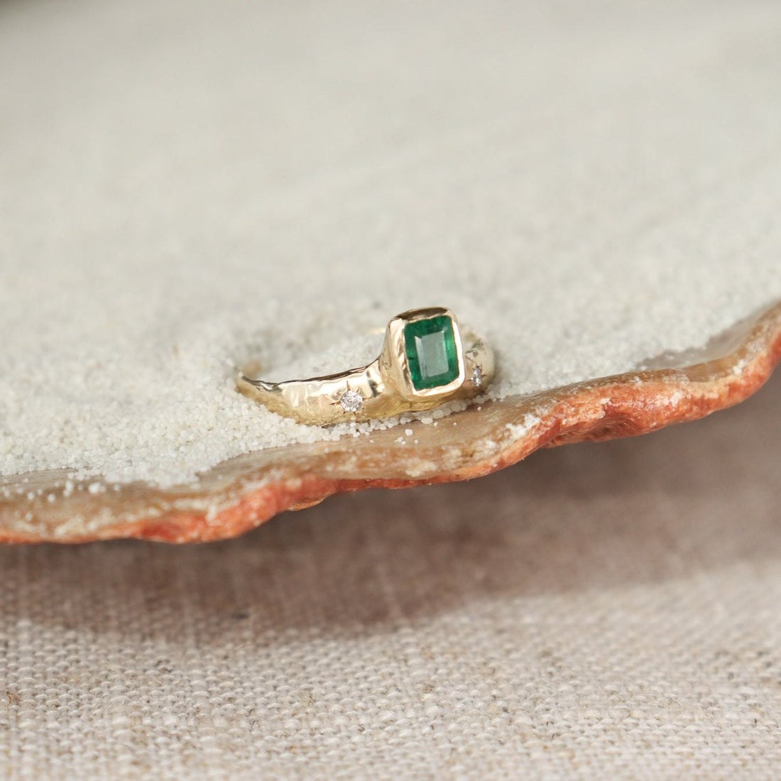 An emerald cut  emerald is bezel set in 14k gold  on a wide band with two star set diamonds on the side of the main stone.